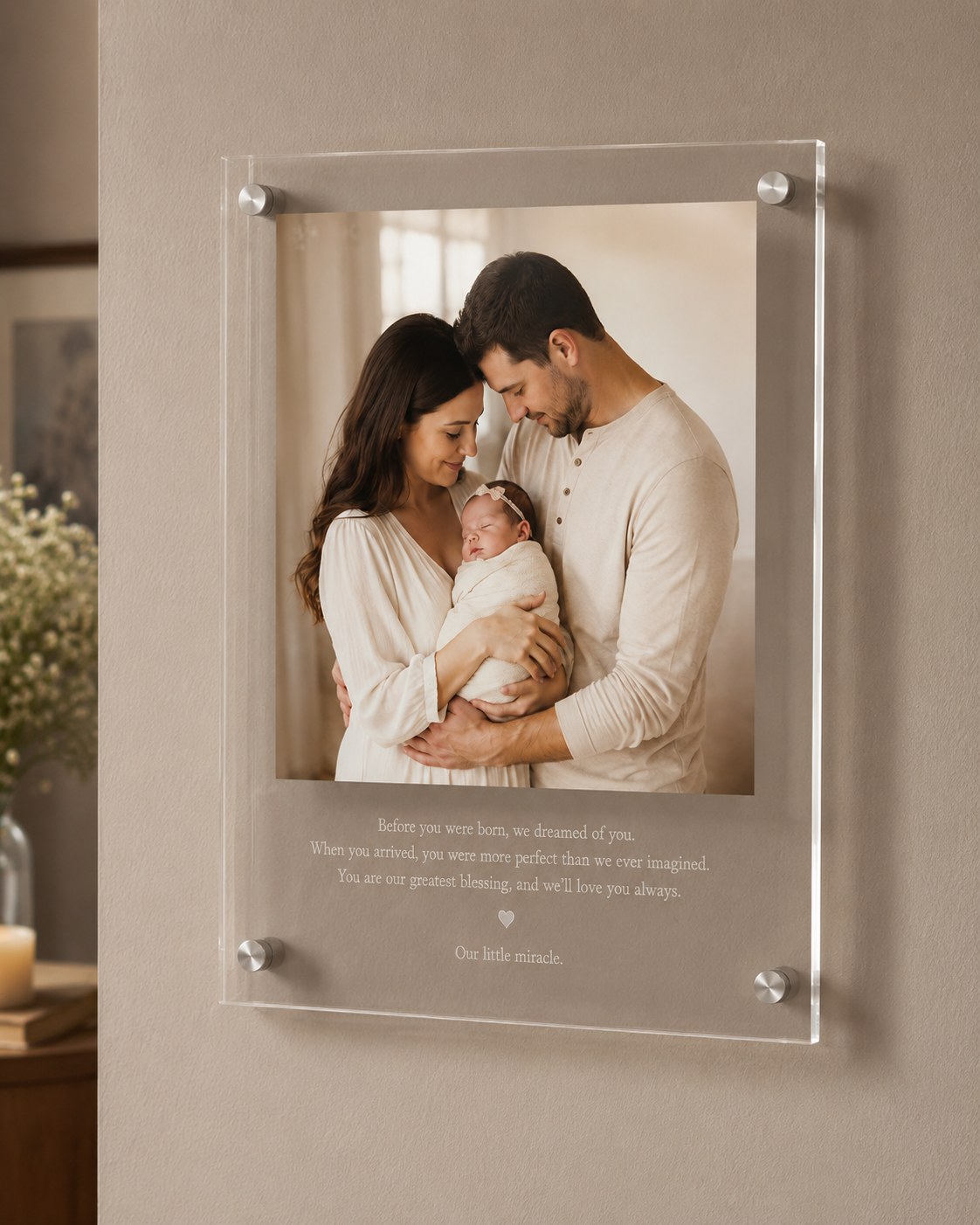 Sample piece from our studio: a new-baby frame with parents holding a newborn in soft window light and a welcome toast printed beneath, mounted on a wall
